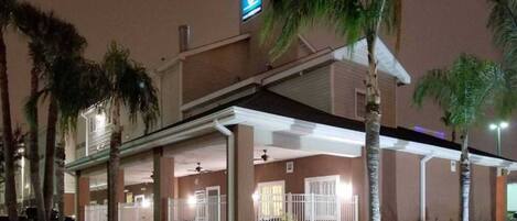 A hotel with a covered outdoor area, palm trees, and a sign indicating a restaurant.