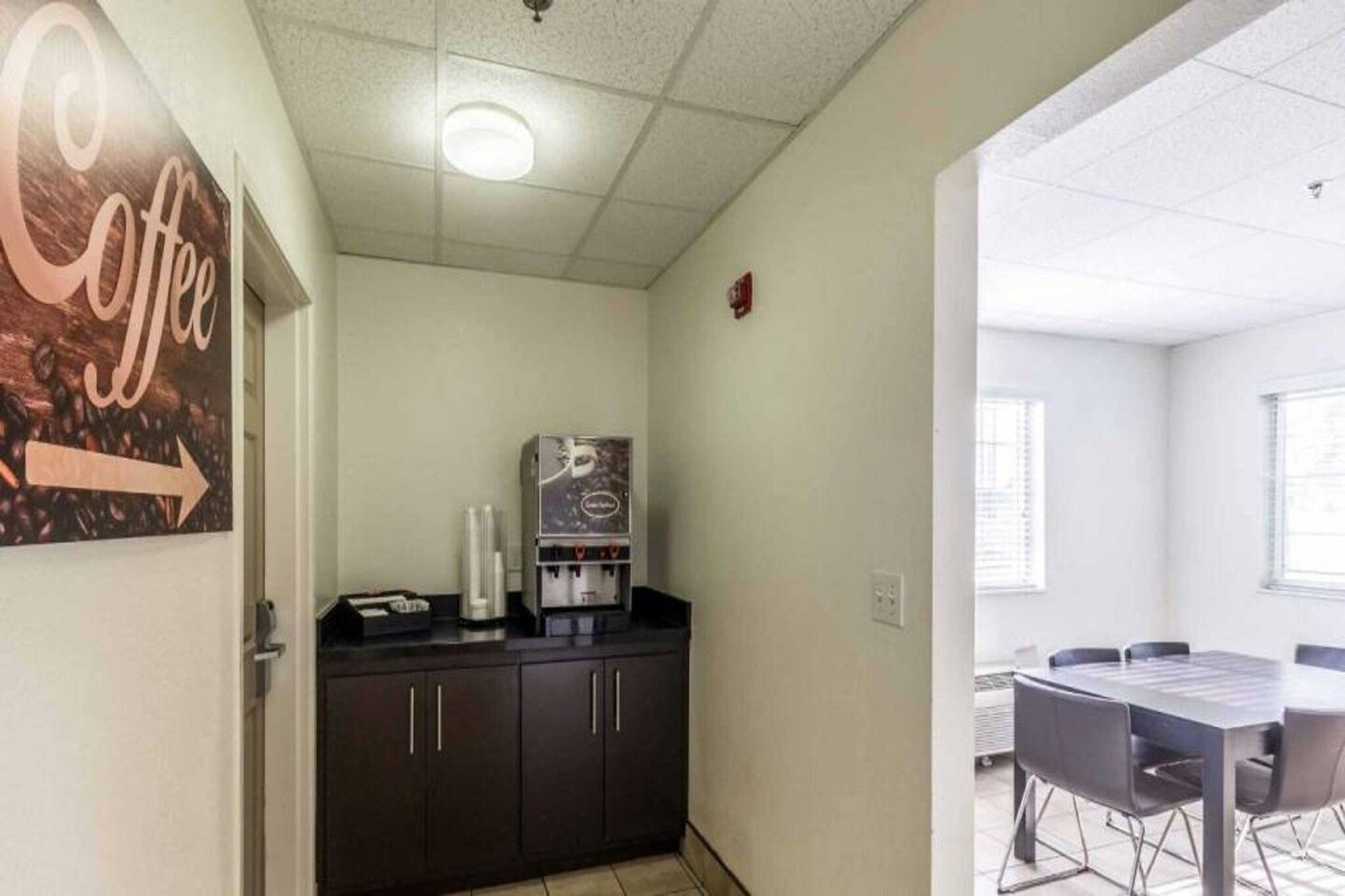 A small office space with a coffee machine, a bulletin board with a coffee sign, and a meeting table with chairs.