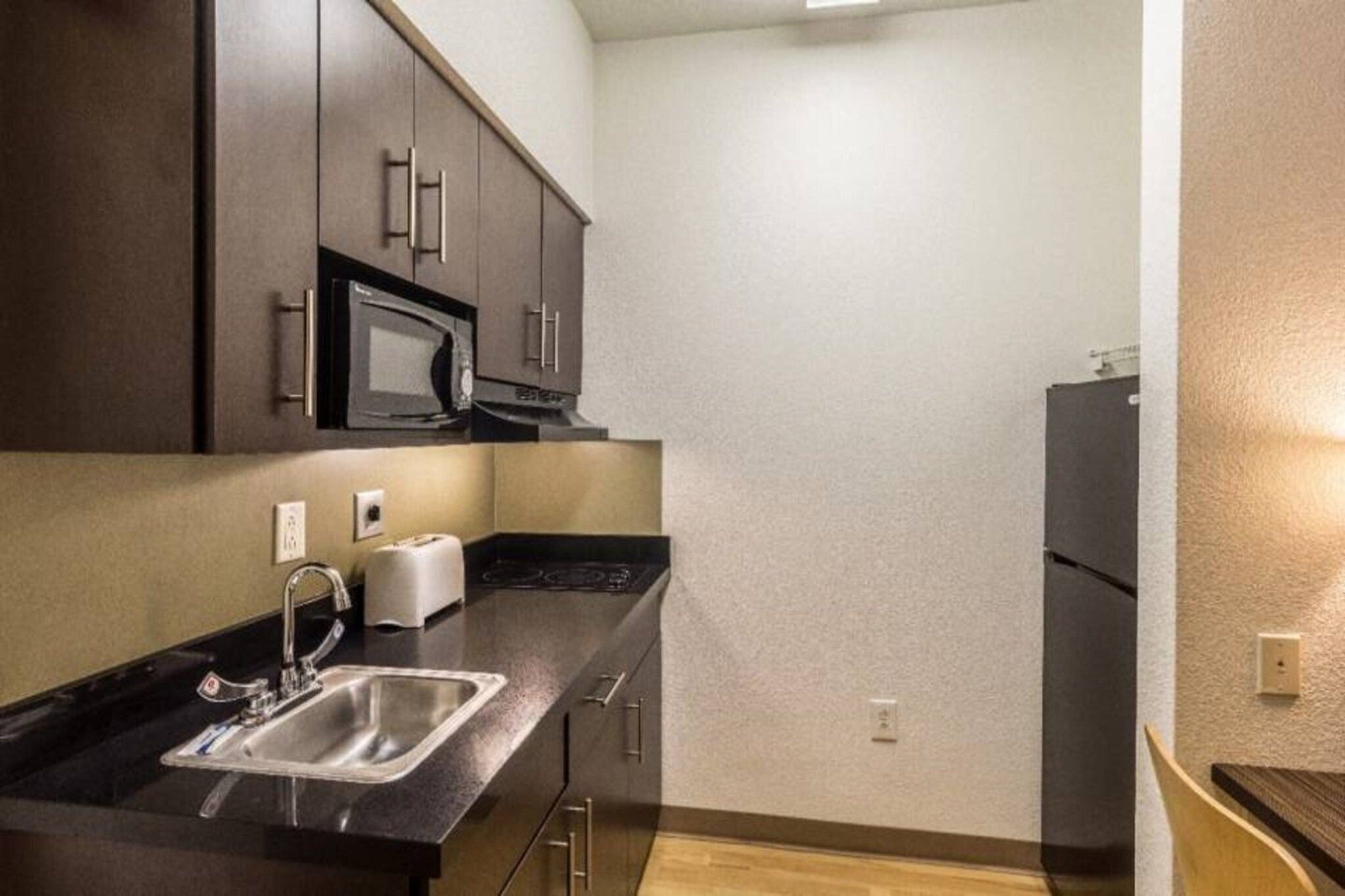 A compact kitchen with a microwave, toaster, sink, and a refrigerator.