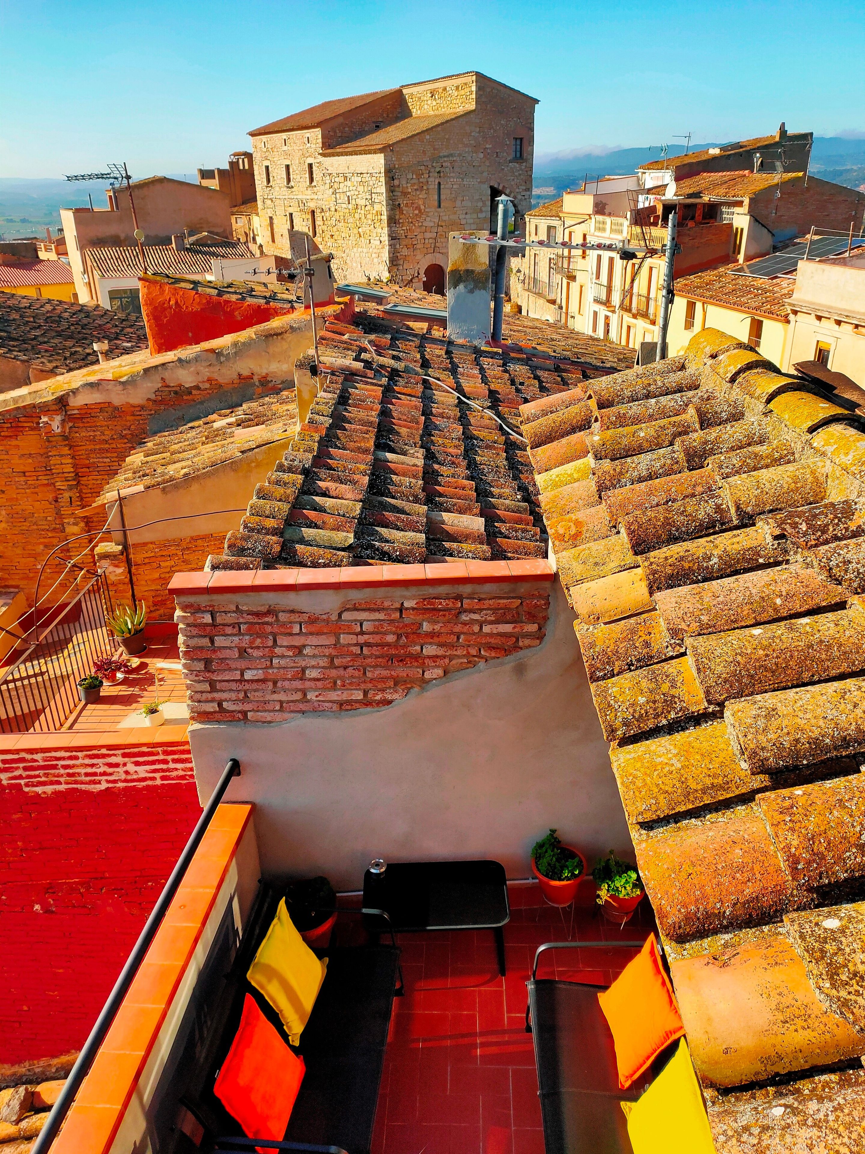 Una terraza en la azotea con un muro de ladrillo, un rincón de descanso con cojines y vistas a la ciudad.