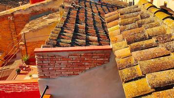Una terraza en la azotea con un muro de ladrillo, un rincón de descanso con cojines y vistas a la ciudad.