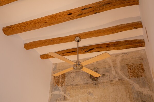 A ceiling fan with wooden beams and a stone wall.
