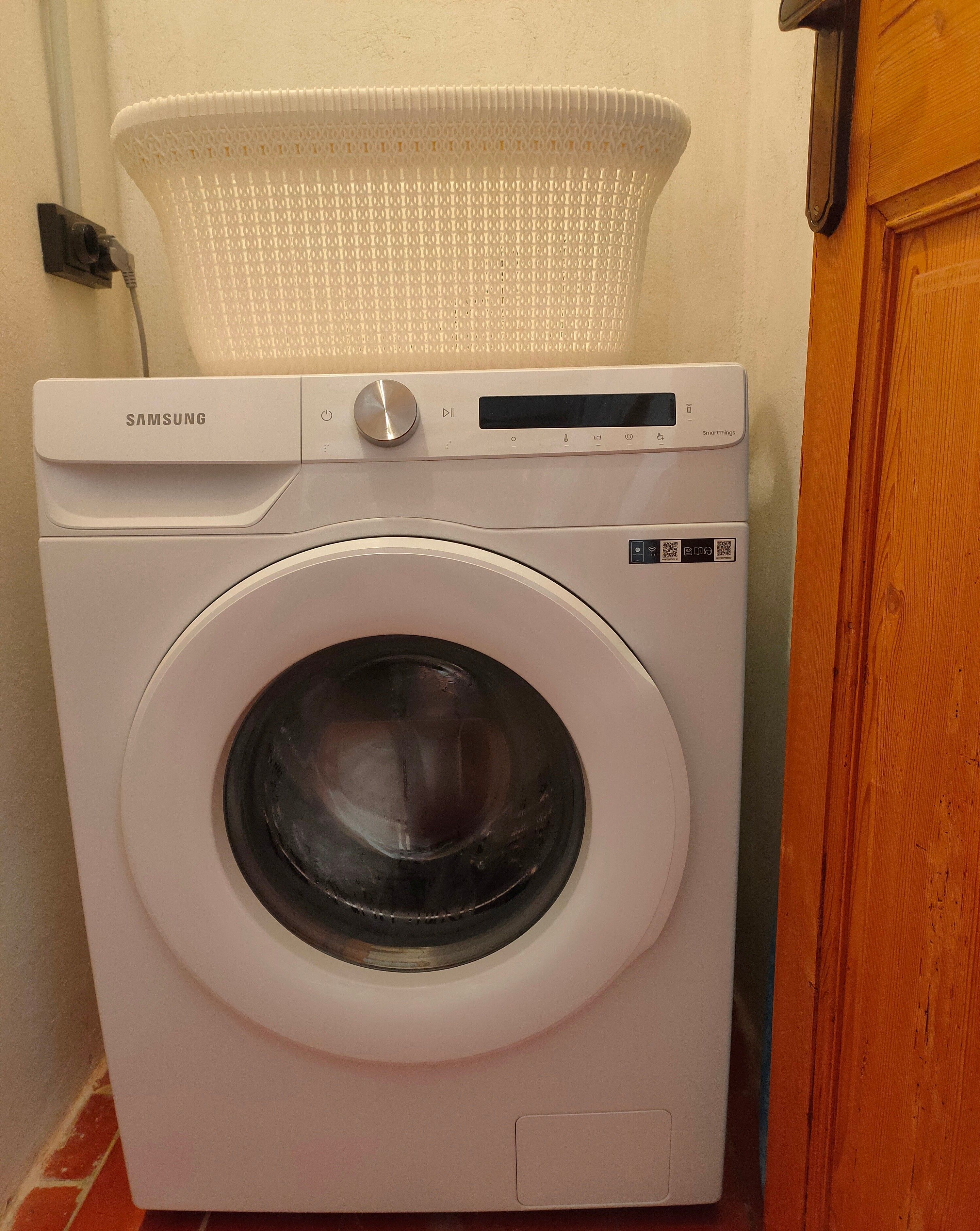 Un lave-linge Samsung SmartThings à chargement frontal, doté d’un panneau de commande et d’un panier situé sur le dessus.