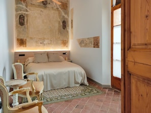 Un dormitorio con una cama, una silla, un tapete estampado y una puerta de madera.