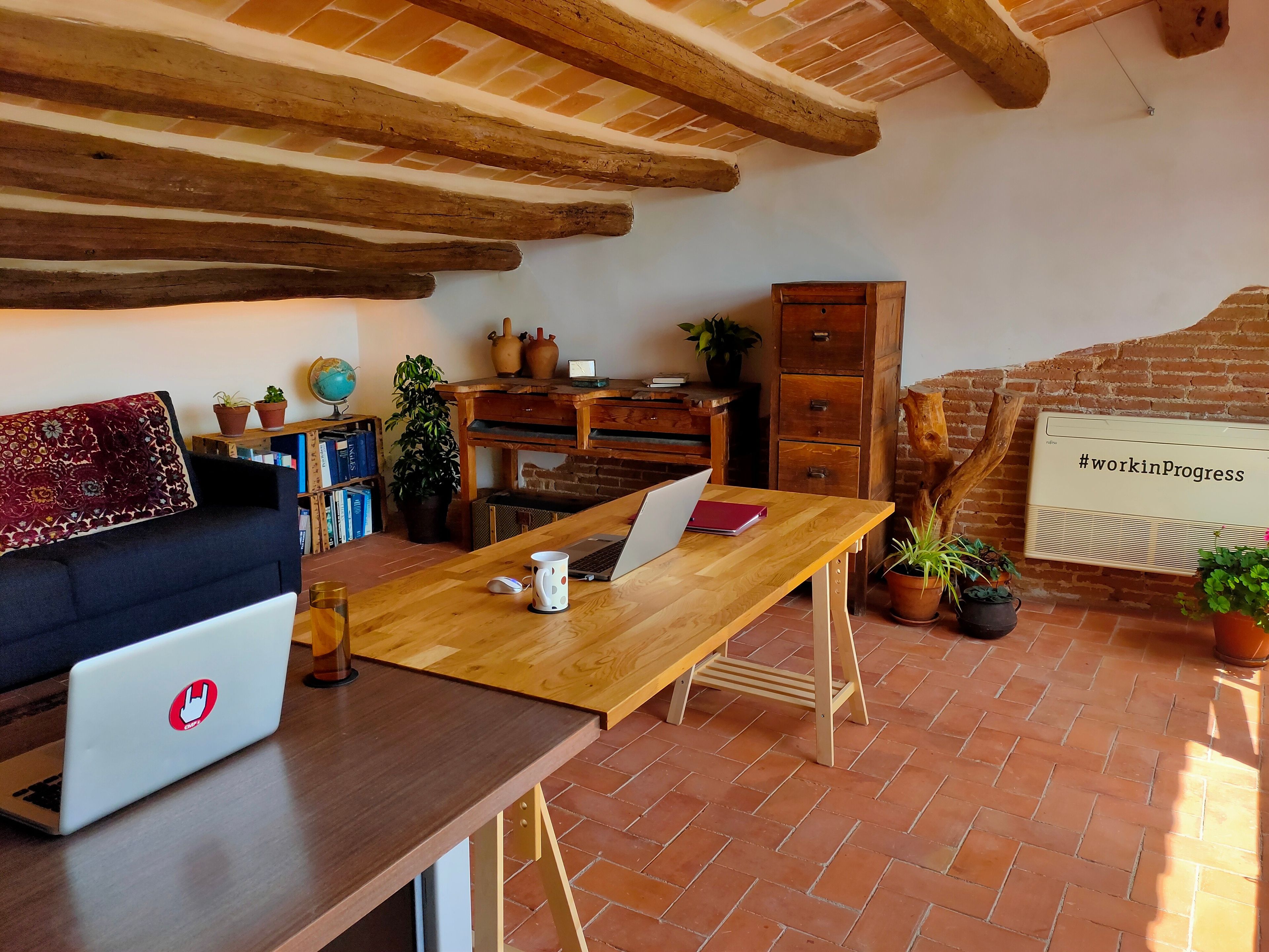Una habitación rústica con un escritorio de madera, una computadora portátil, un sofá y una pared de ladrillo.