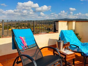 A balcony with two chairs, a table, and a view of the countryside.