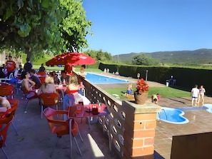 Un área de comedor al aire libre con mesas y sillas, una piscina y vistas del paisaje.