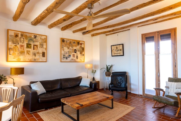 Una sala de estar con techo de madera, un sofá de cuero negro, una mesa de centro de madera y un collage enmarcado en la pared.