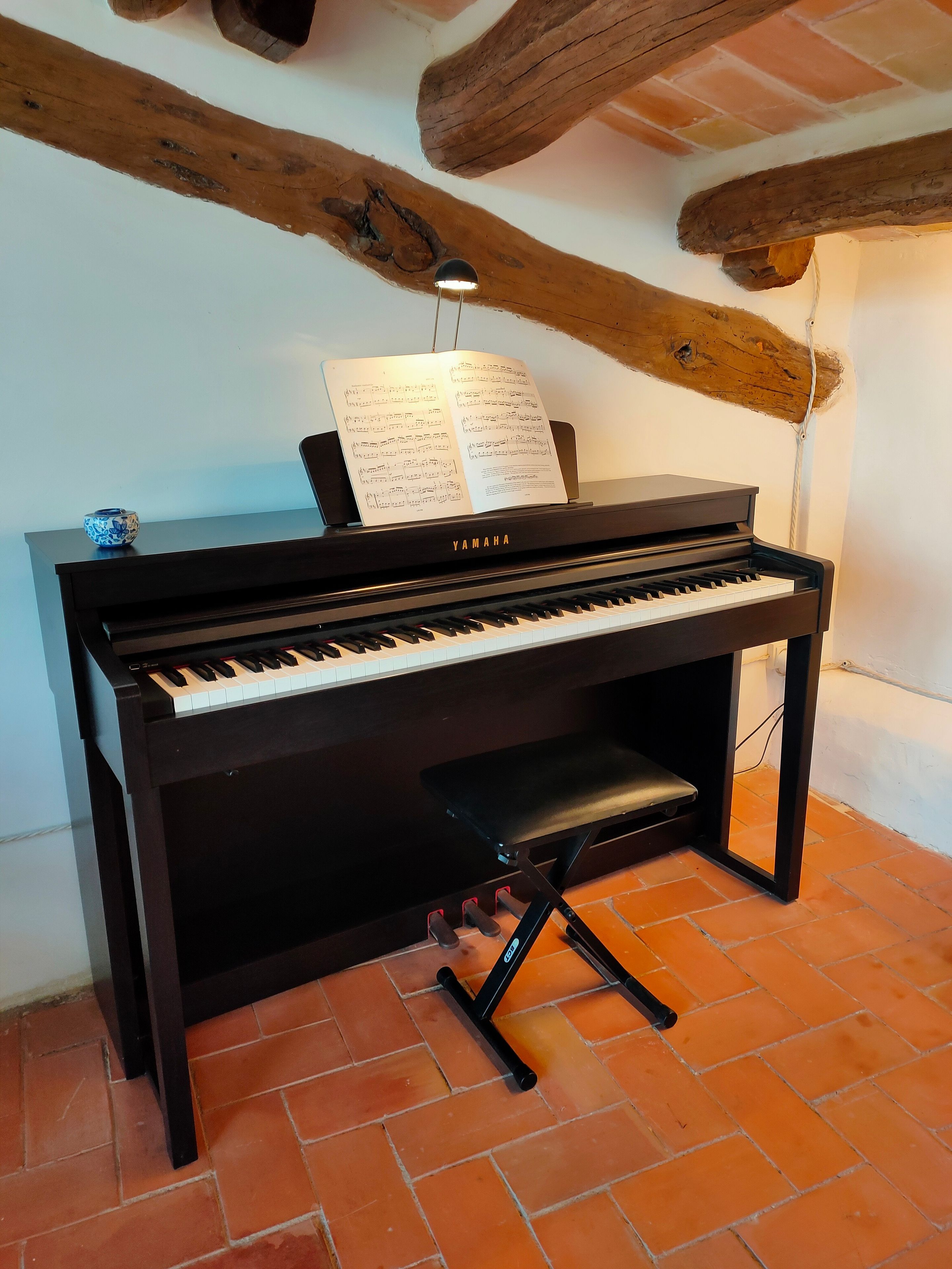 Ein Yamaha-Klavier mit Noten darauf, eine Bank und ein Notenständer davor.