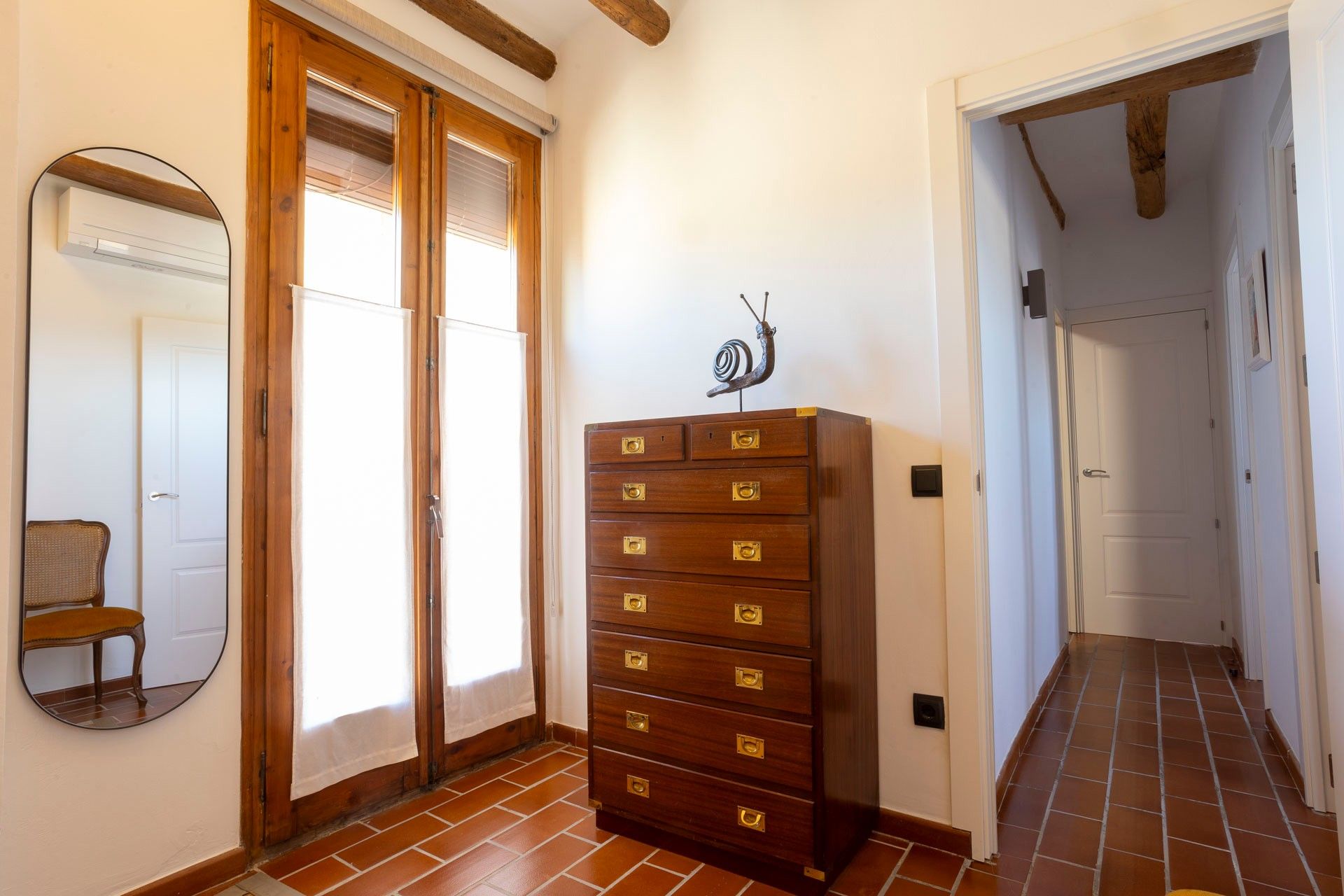 Een gang met een houten dressoir met meerdere laden en een spiegel aan de muur.
