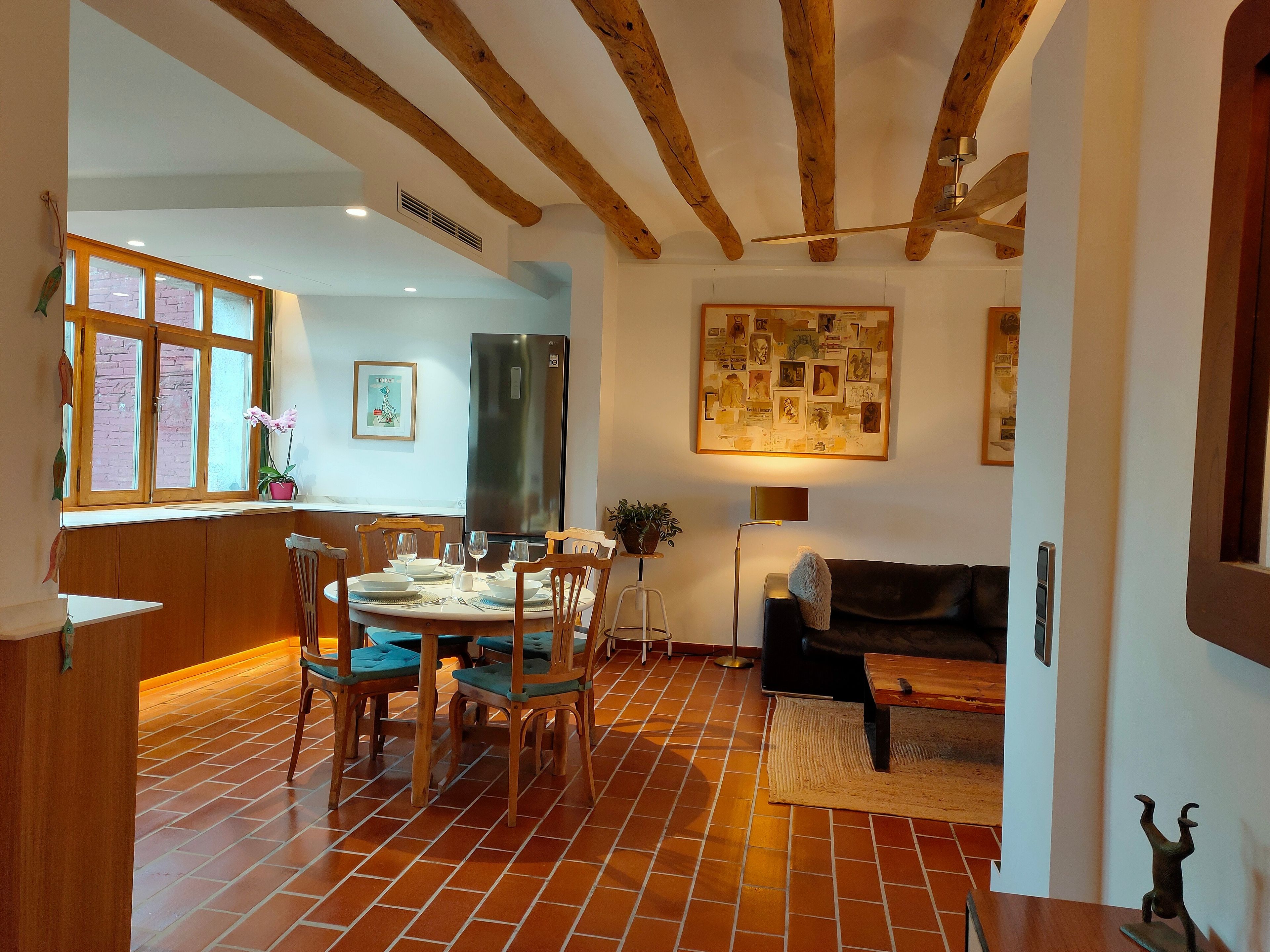 A dining area with a wooden table and chairs, a refrigerator, and a wall with a collage of pictures.