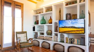 A living room with a television, shelves with decorative items, a chair, and a rustic wooden chair.