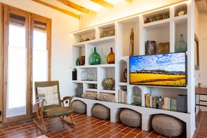 A living room with a television, shelves with decorative items, a chair, and a rustic wooden chair.