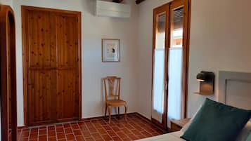 Una habitación con una cama, un armario de madera, una silla, aire acondicionado instalado en la pared y una ventana con persianas.