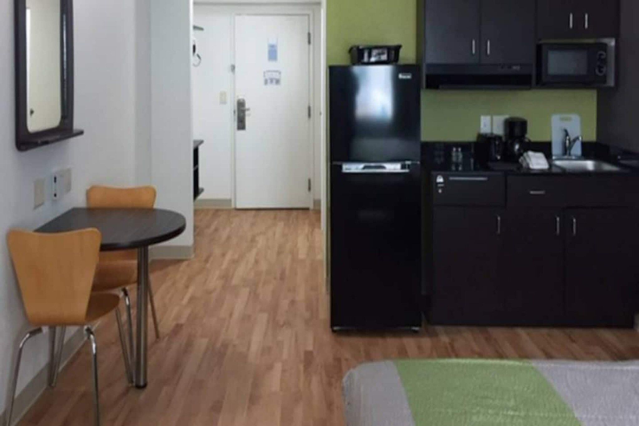 A compact kitchen with a refrigerator, microwave, and sink. There is a small dining area with a table and two chairs.