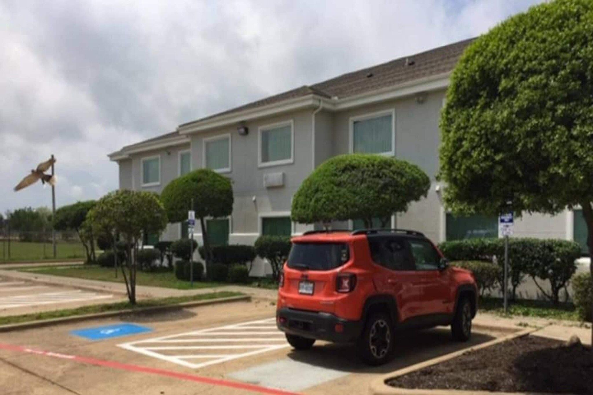 A parking lot with a red SUV, a crosswalk, and a building with a flat roof and multiple windows.