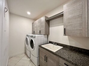 A laundry room with a washing machine and dryer, a sink, and wooden cabinets. - Pickleball/Gameroom/Soccer Field/Pool (Miami)