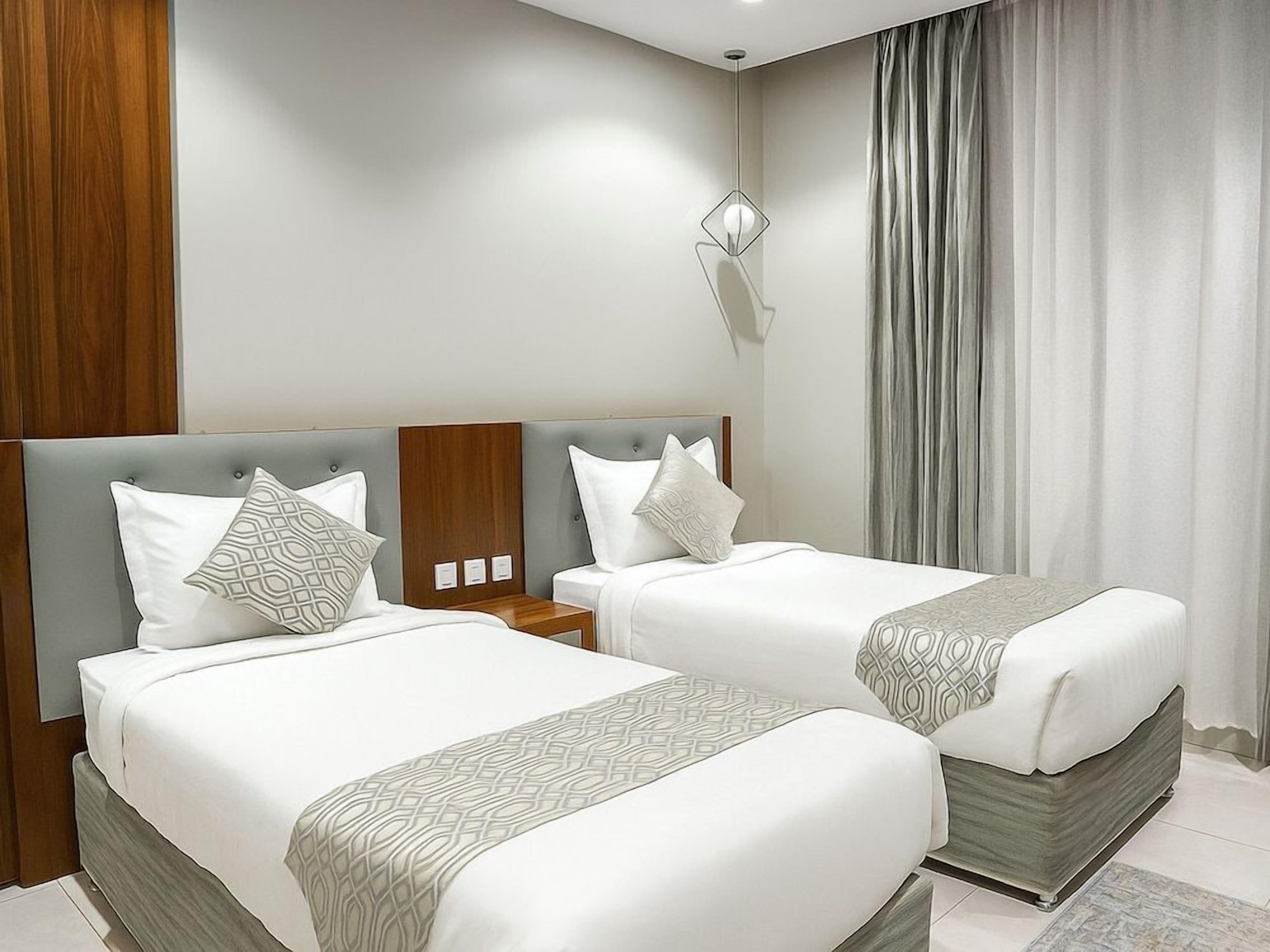 A hotel room with two beds, a modern headboard, a nightstand, and a large window with curtains.