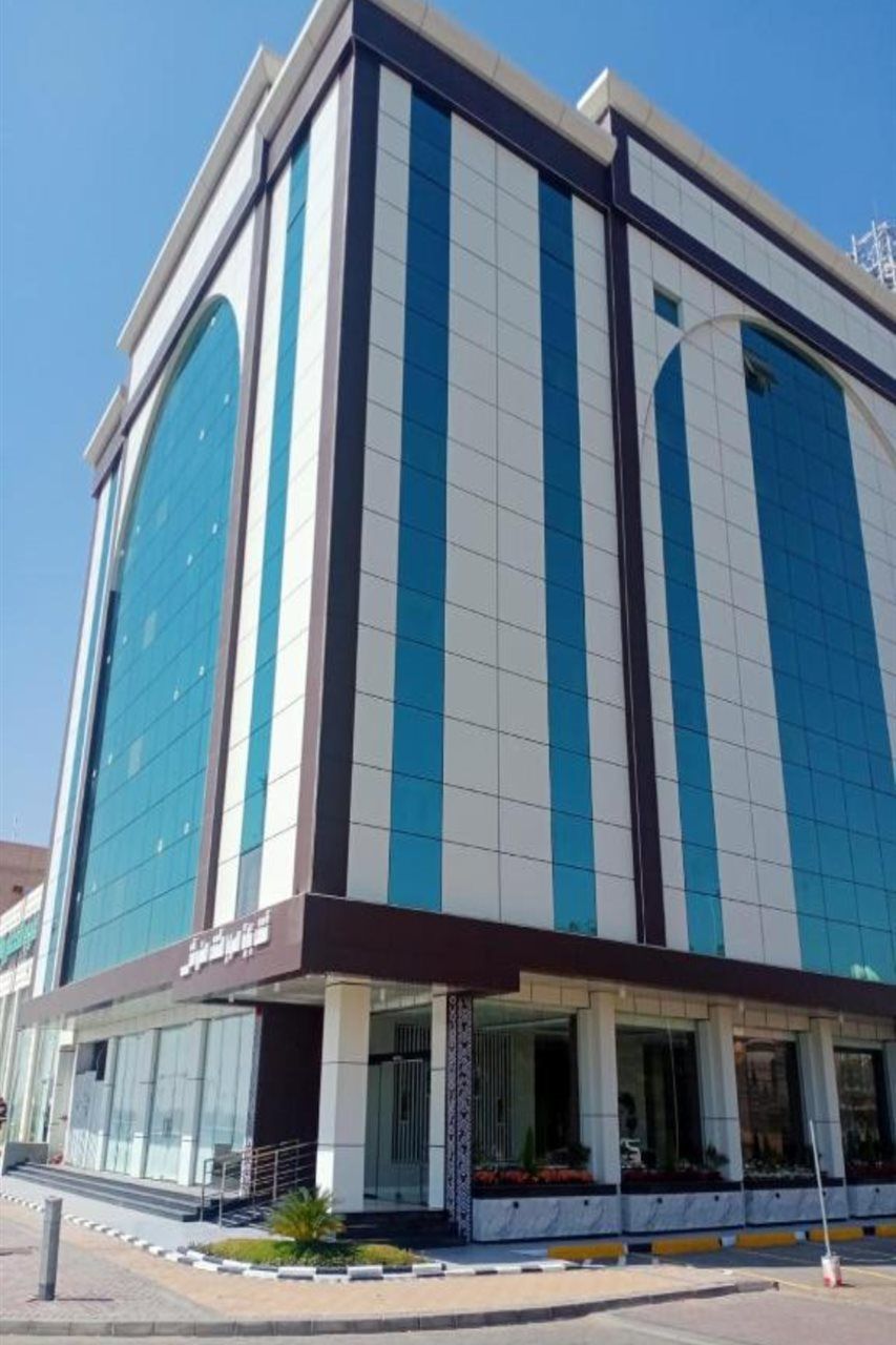 A modern building with a large glass facade, a prominent entrance with a covered area, and a clear sky in the background.