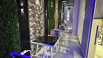 A corridor with a stone wall, green foliage, and a series of tables and chairs.