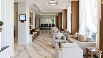 A modern hotel lobby with a reception desk, seating area, and a view of the dining area.