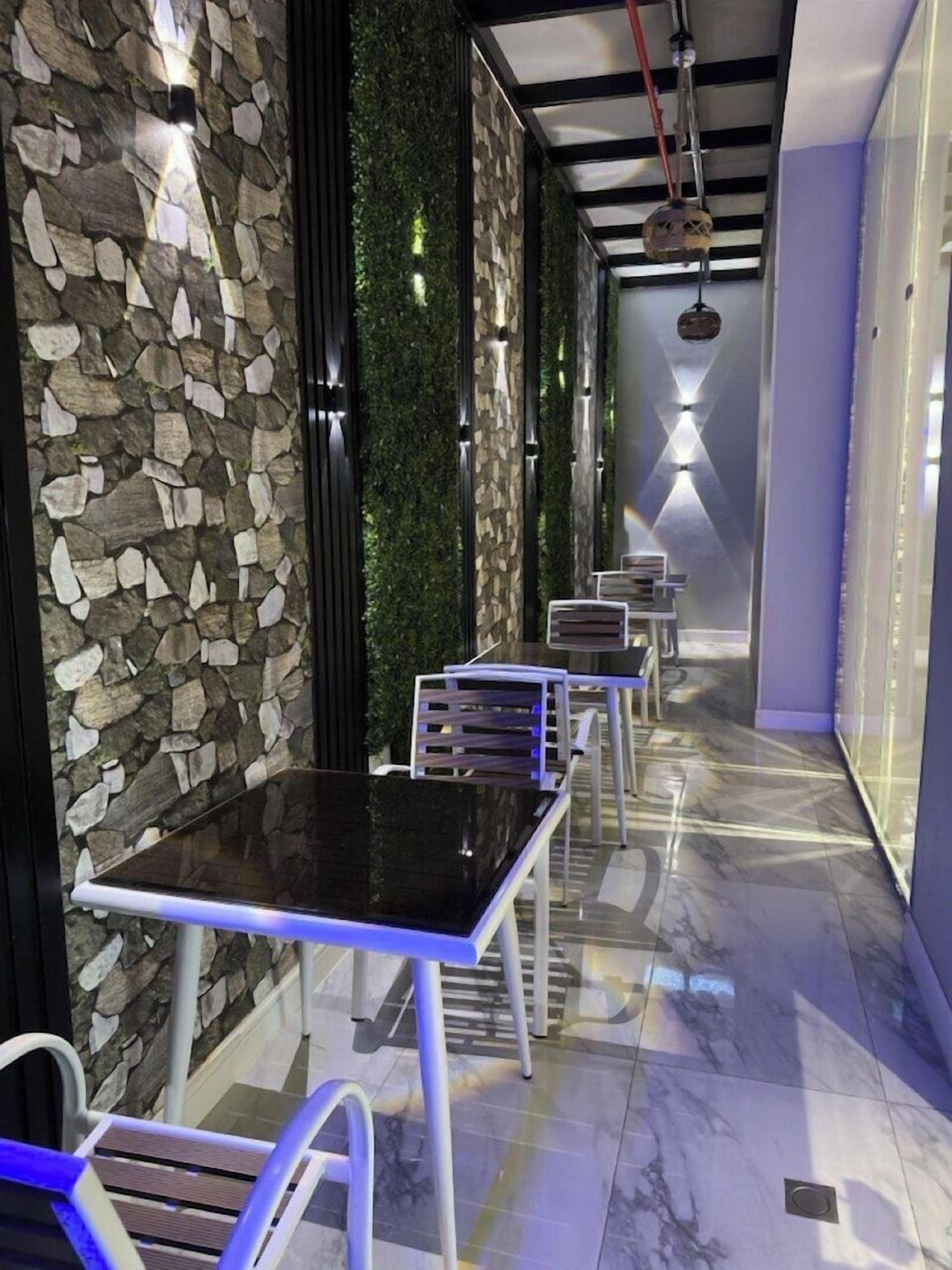 A corridor with stone walls, green walls, and a marble floor. There are tables and chairs along the corridor.