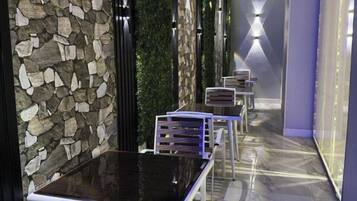 A corridor with stone walls, green walls, and a marble floor. There are tables and chairs along the corridor.