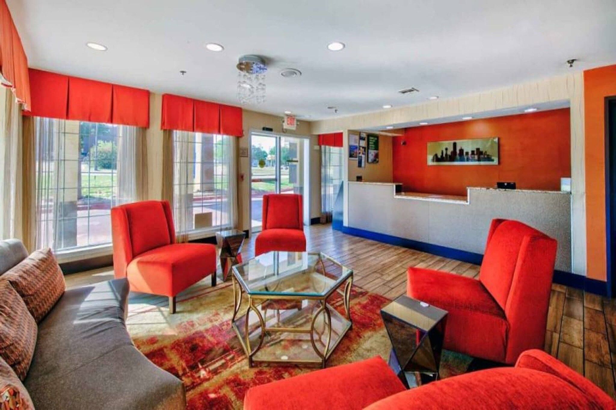 A hotel lobby with red chairs, a glass coffee table, and a reception desk.