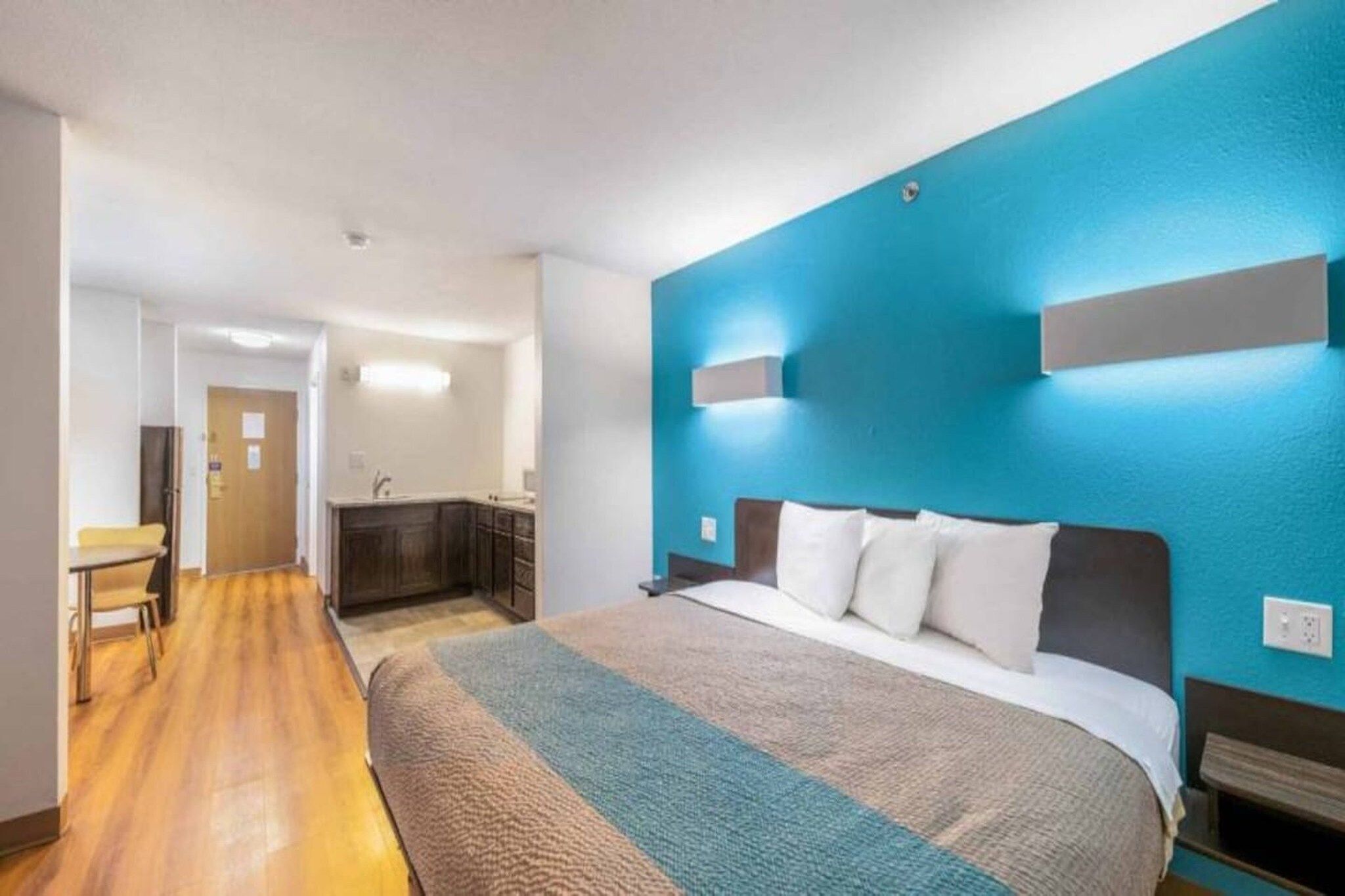 A hotel room with a large bed, a desk, and a kitchenette.