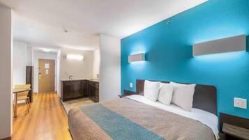 A hotel room with a large bed, a desk, and a kitchenette.
