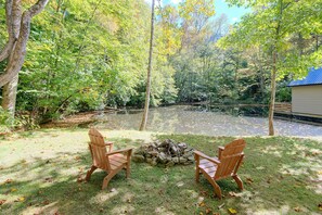 A serene outdoor seating area with two wooden chairs facing a small fire pit surrounded by a natural setting. - Walden Cove: A Peaceful Floating Retreat on a Pond (Maggie Valley)