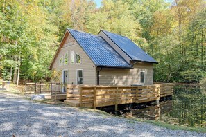 Eine Holzhütte mit Metalldach, einer Holzterrasse und einem Teich im Hintergrund.