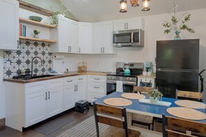 Une cuisine moderne avec des meubles blancs, un réfrigérateur en acier inoxydable et une table à manger bleue agrémentée de sets de table en fibres tressées.