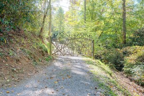 Un chemin de gravier mène à un portail en métal situé dans une zone boisée.