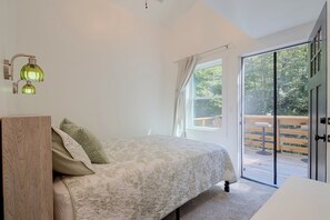Ein Schlafzimmer mit Bett, Nachttisch, einem Fenster mit Vorhängen und Blick auf einen Balkon.