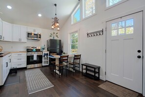 A kitchen with white cabinets, a stainless steel oven, a microwave, and a black refrigerator. There is a dining table with chairs and a small bench. - Walden Cove: A Peaceful Floating Retreat on a Pond (Maggie Valley)