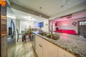 A modern kitchen with a stainless steel refrigerator, granite countertops, and a red pool table. - Walkable Main St Retreat! 5 Mi to Mount Pleasant (Cambridge Springs)