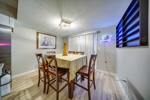 A dining area with a table set for four, wooden chairs, a framed picture on the wall, and a neon sign. - Walkable Main St Retreat! 5 Mi to Mount Pleasant (Cambridge Springs)