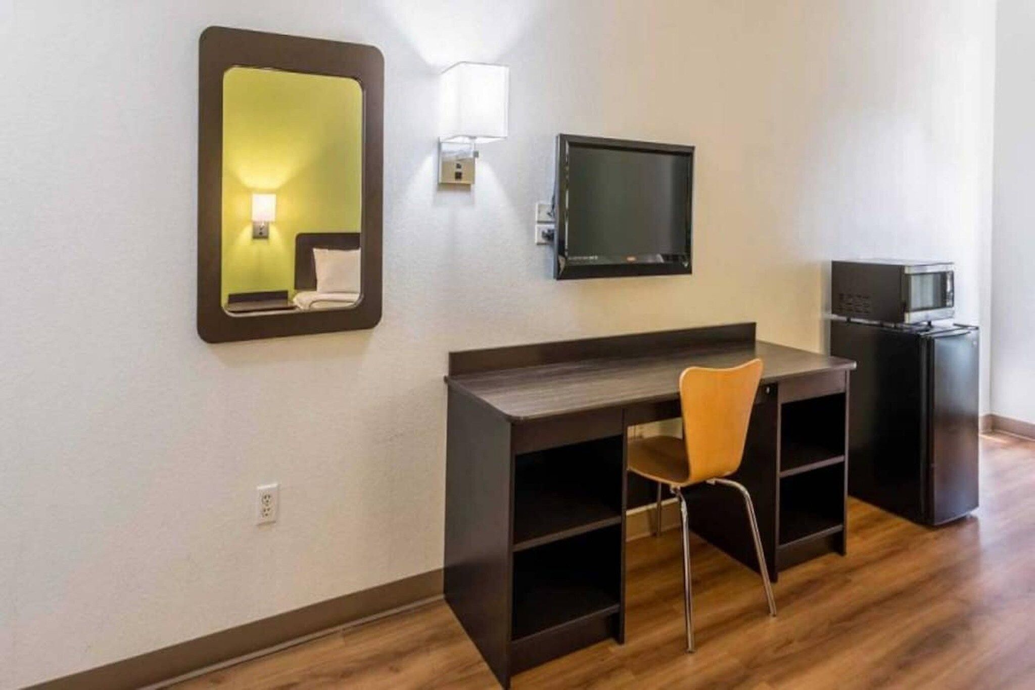 Una habitación de hotel con un escritorio de madera, una silla, un televisor, un microondas y un espejo.