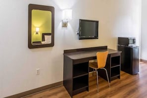 Una camera d'albergo con una scrivania in legno, una sedia, una televisione, un forno a microonde e uno specchio.