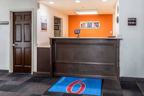 Un'area reception con una scrivania marrone, un tappeto blu con il numero 6 rosso e un muro con cartelli numerati.