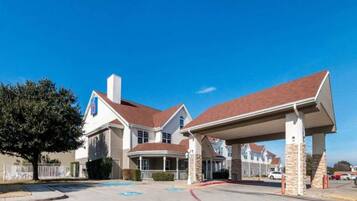 A two-story building with a covered parking area and a large tree in the foreground.