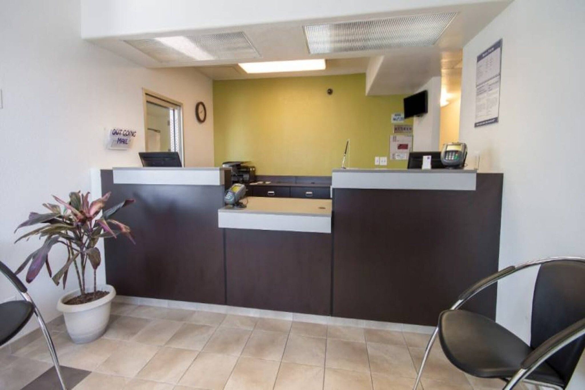 A reception desk with a computer, a telephone, and a plant. There are chairs and a clock on the wall.