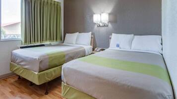 Una habitación de hotel con dos camas, una ventana con cortinas, una lámpara de pared y suelo de madera.