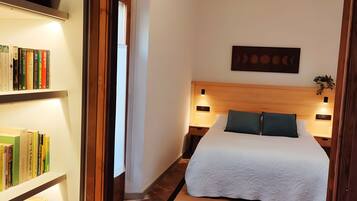 A hotel room with a bed, bedside lamps, a bookshelf, and a wall-mounted artwork.