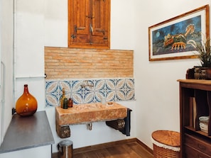 A kitchen with a tiled backsplash, a wooden cabinet, a sink, and a painting on the wall.