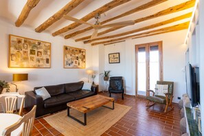 A living room with exposed wooden beams, a brown leather sofa, a wooden coffee table, and a television on a stand.