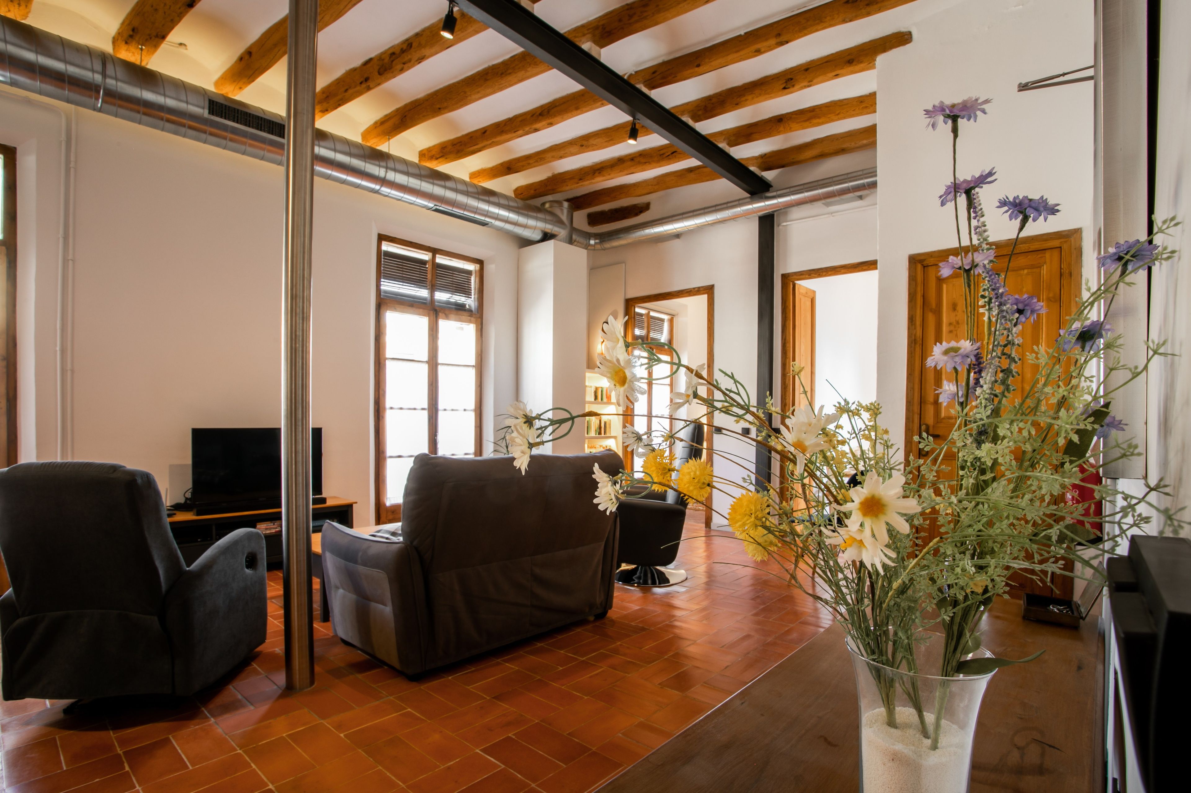 Uma sala de estar com lareira, sofá, televisão e um vaso de flores.
