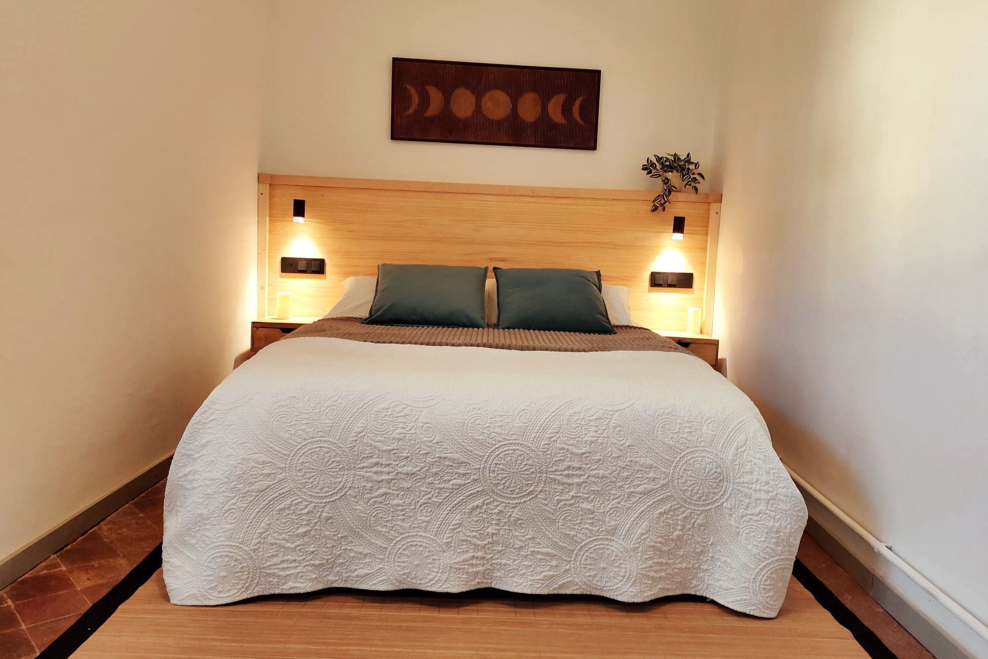Un lit bien fait, recouvert d’une couvre-lit à motifs, avec deux lampes de chevet de chaque côté et une tête de lit en bois.