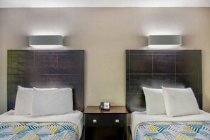 A hotel room with two beds, each with white bedding and a patterned duvet. There are two bedside tables with lamps, and a small table between the beds with a telephone. - Spacious 2 Queen Beds | Nsmk, Micfridge (ARLINGTON)